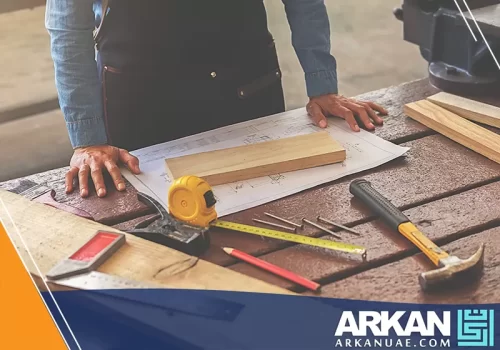 جار تركيب أثاث في دبي وهو يعمل على قياس وتخطيط الخشب باستخدام أدوات القياس والرسومات الفنية.