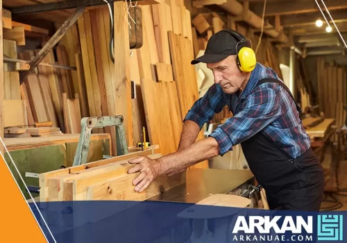 نجار في دبي يعمل في ورشة نجارة، حيث يقوم بتقطيع الأخشاب باستخدام معدات النجارة، مع التركيز على دقة العمل.